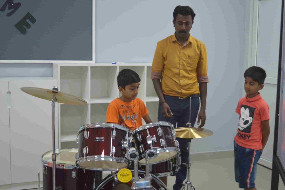 A boy practising drums with the help of a music teacher at CMIS.