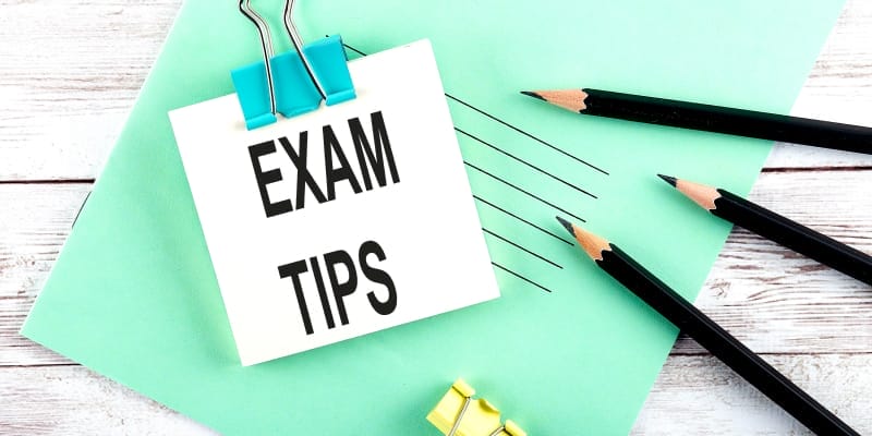Exam tips written on short paper with black pencils on the side and a light blue file are placed underneath the paper.