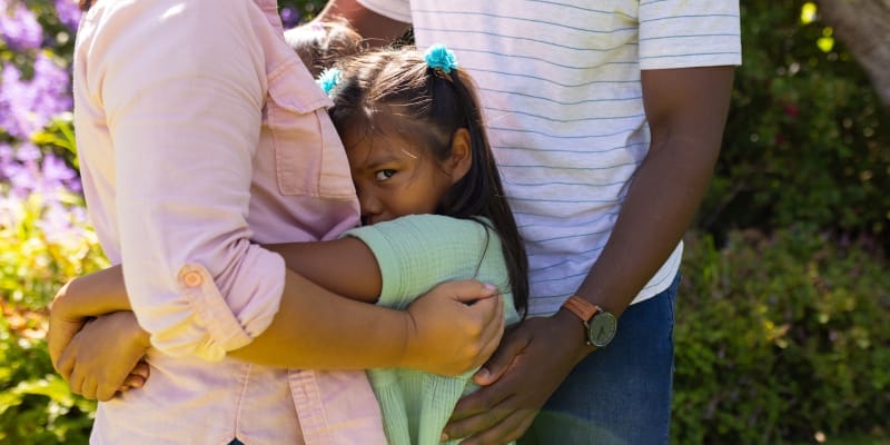 Supportive parents hugging their shy daughter, illustrating how to help children overcome anxiety for interviews.